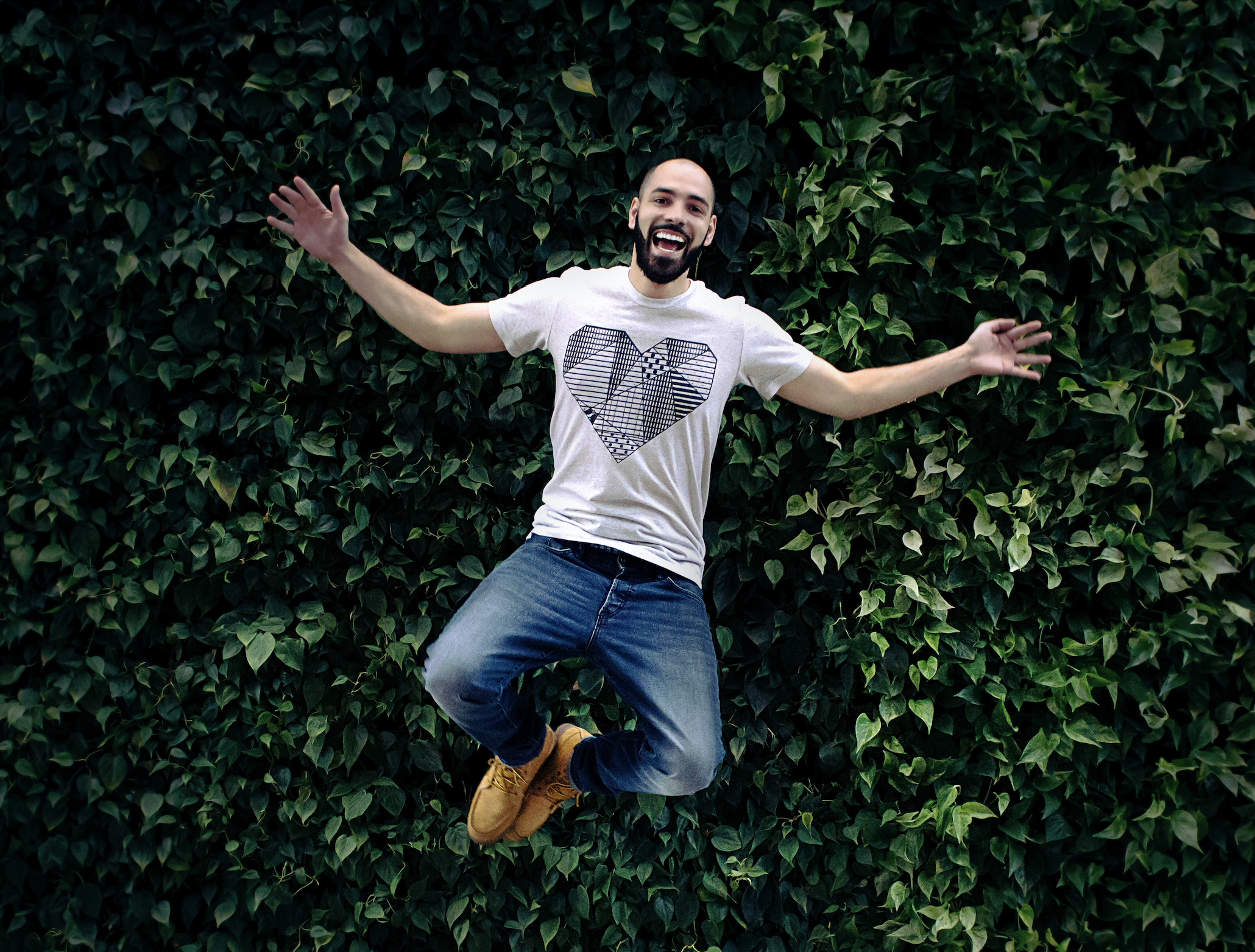 man jumping with arms out to the side in front of plant background